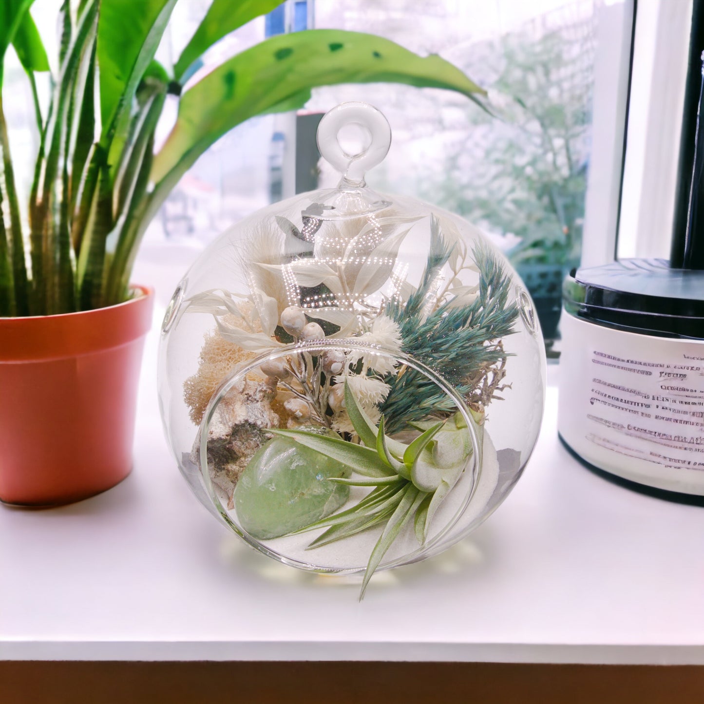 Glass bubble terrarium with sand, dried flowers, an airplant and a polished green fluorite stone
