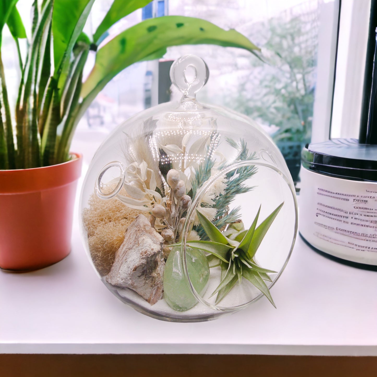 Glass bubble terrarium with sand, dried flowers, an airplant and a polished green fluorite stone