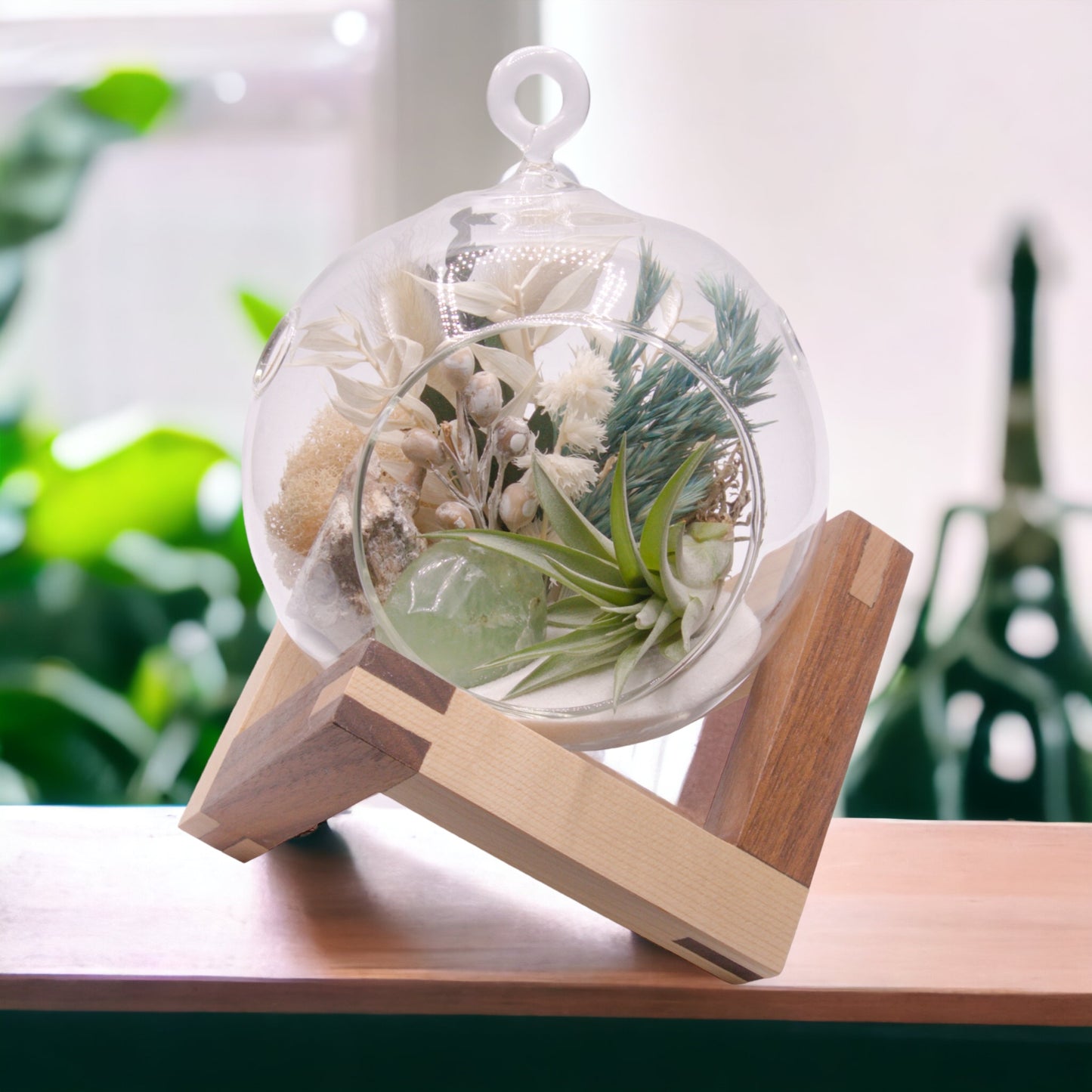 Glass bubble terrarium with sand, dried flowers, an airplant and a polished green fluorite stone