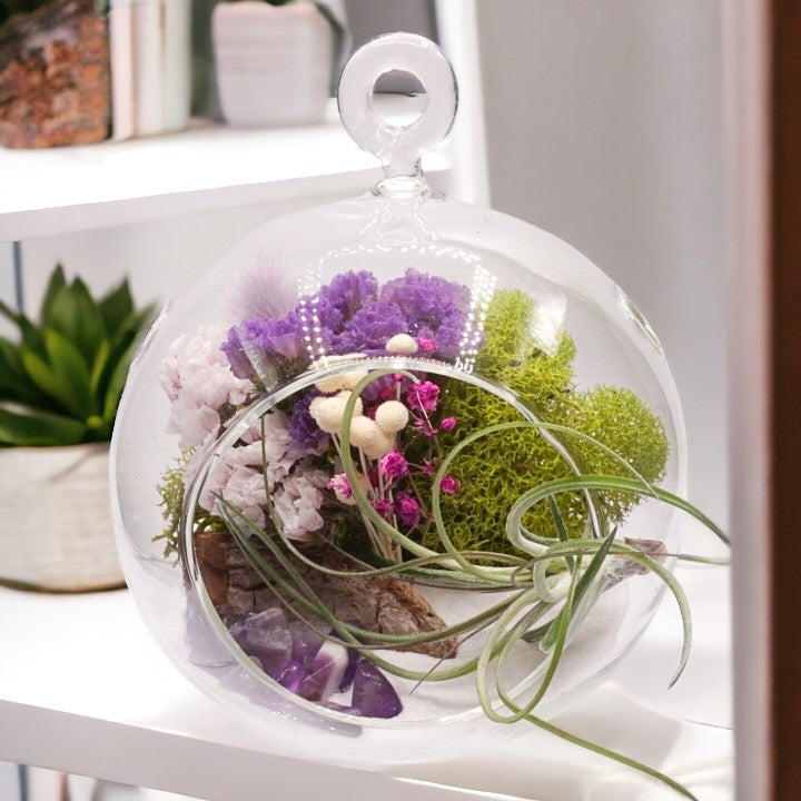 Glass bubble airplant terrarium with purple dried flowers, sand, moss, wood, amethyst crystals and an airplant