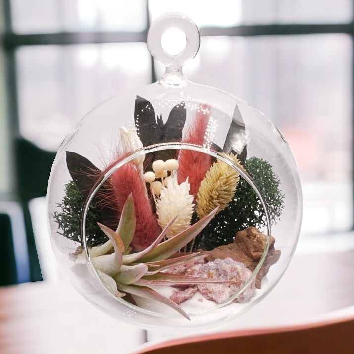 Glass bubble airplant terrarium with pink dried flowers, sand, moss, wood, rose quartz or pink tourmaline crystals and an airplant