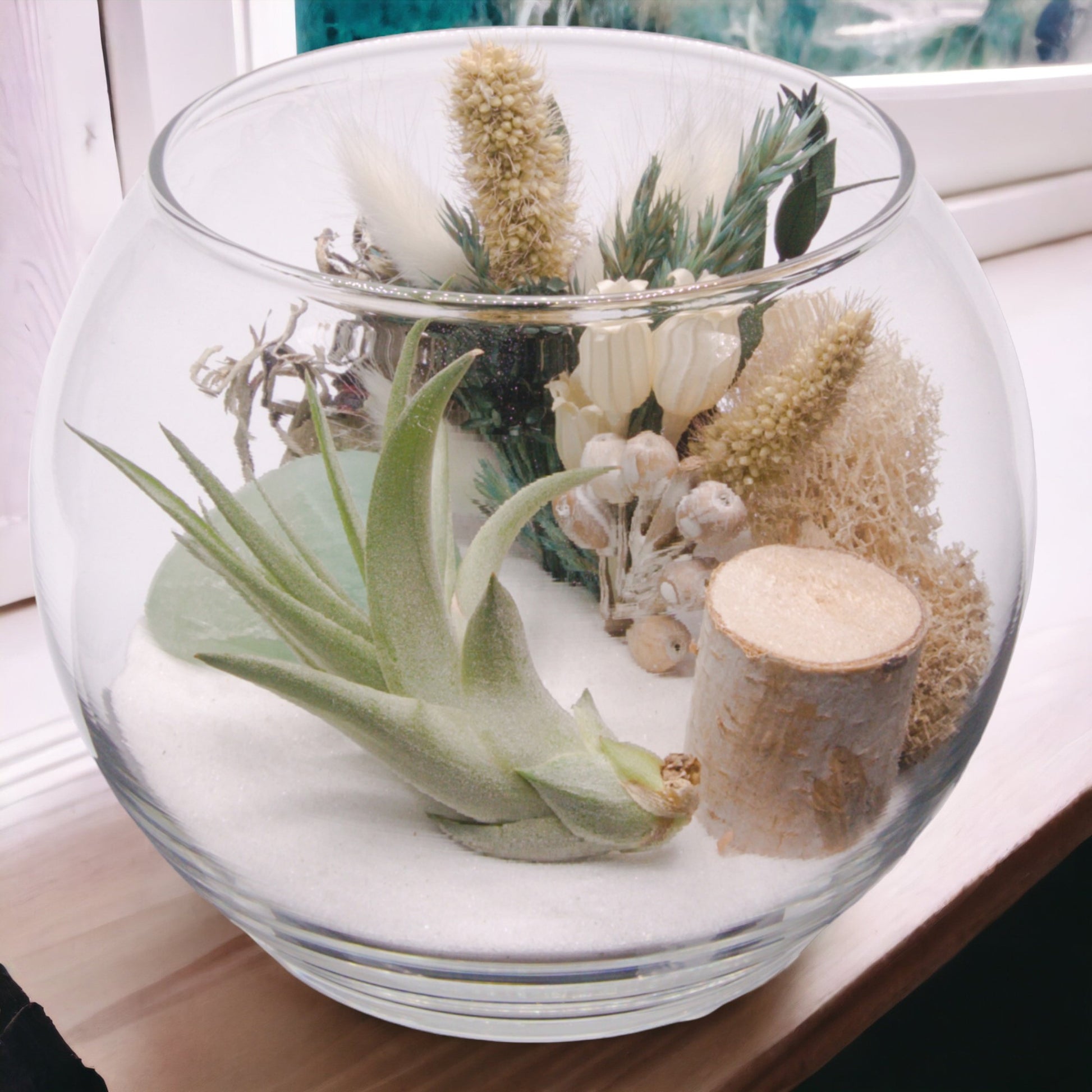 Glass bowl terrarium with dried flowers, moss, sand, an airplant and a green fluorite crystal