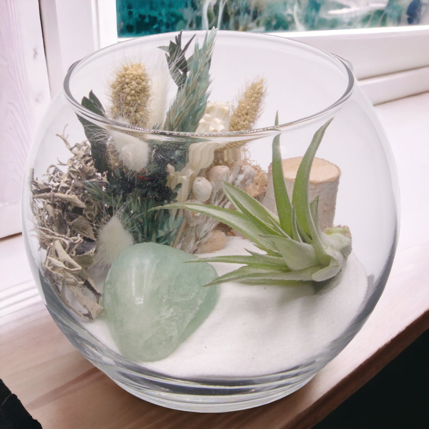 Glass bowl terrarium with dried flowers, moss, sand, an airplant and a green fluorite crystal