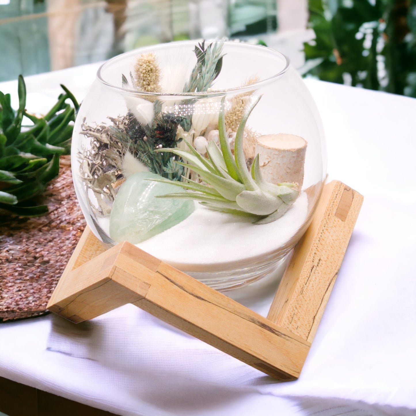 Glass bowl terrarium with dried flowers, moss, sand, an airplant and a green fluorite crystal