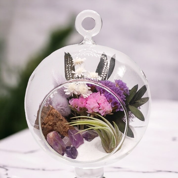 Glass bubble airplant terrarium with purple dried flowers, sand, moss, wood, amethyst crystals and an airplant