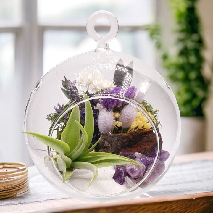 Glass bubble airplant terrarium with purple dried flowers, sand, moss, wood, amethyst crystals and an airplant