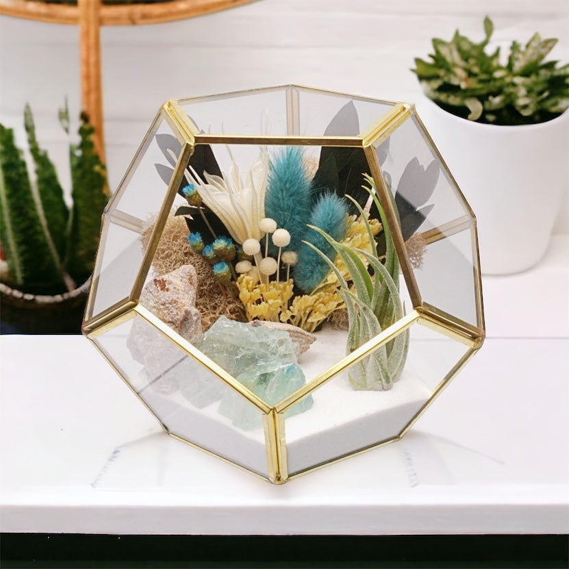Gold-rimmed geometric glass terrarium with an airplant, dried flower bouquet with turquoise accents, sand, moss and green fluorite crystals