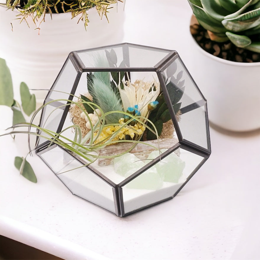 Black-rimmed geometric glass terrarium with an airplant, dried flower bouquet with turquoise accents, sand, moss and green calcite crystals