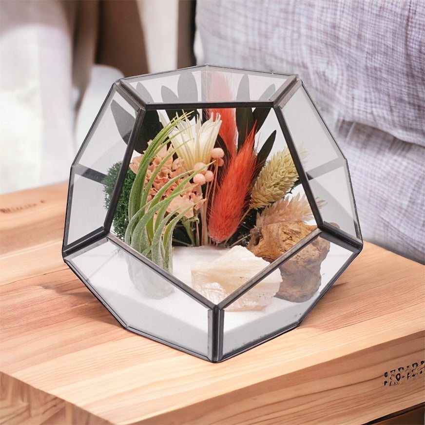 Black-rimmed glass geometric airplant terrarium with peach coloured dried flowers, moss, sand and stilbite crystals