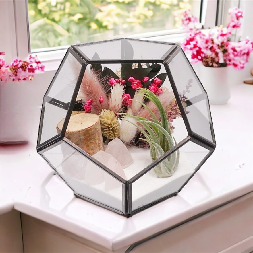Airplant terrarium in a black rimmed geometric glass vase with pink bouquet of dried flowers, moss, wood and rose quartz crystals