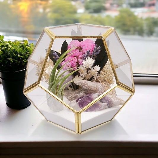 Gold-rimmed glass victorian terrarium with a dried flower bouquet with purple accents, an amethyst chevron crystal, airplant, sand, moss and wood