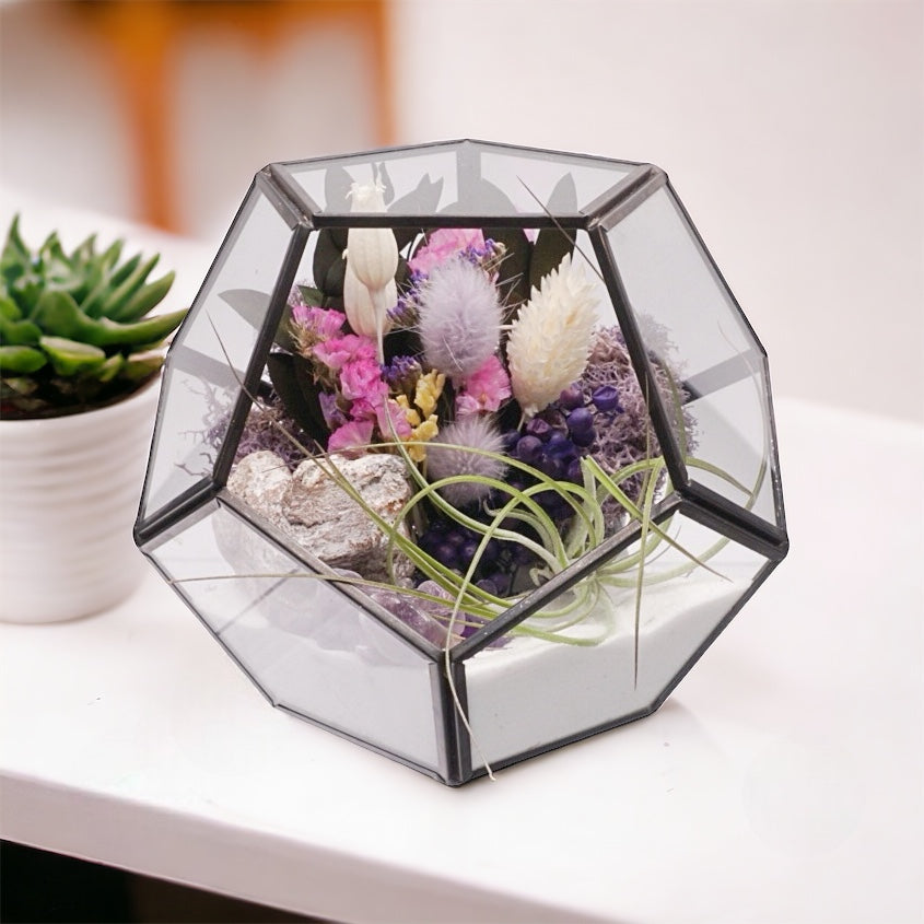 Black-rimmed glass victorian terrarium with a dried flower bouquet with purple accents, polished amethyst crystals, airplant, sand, moss and wood