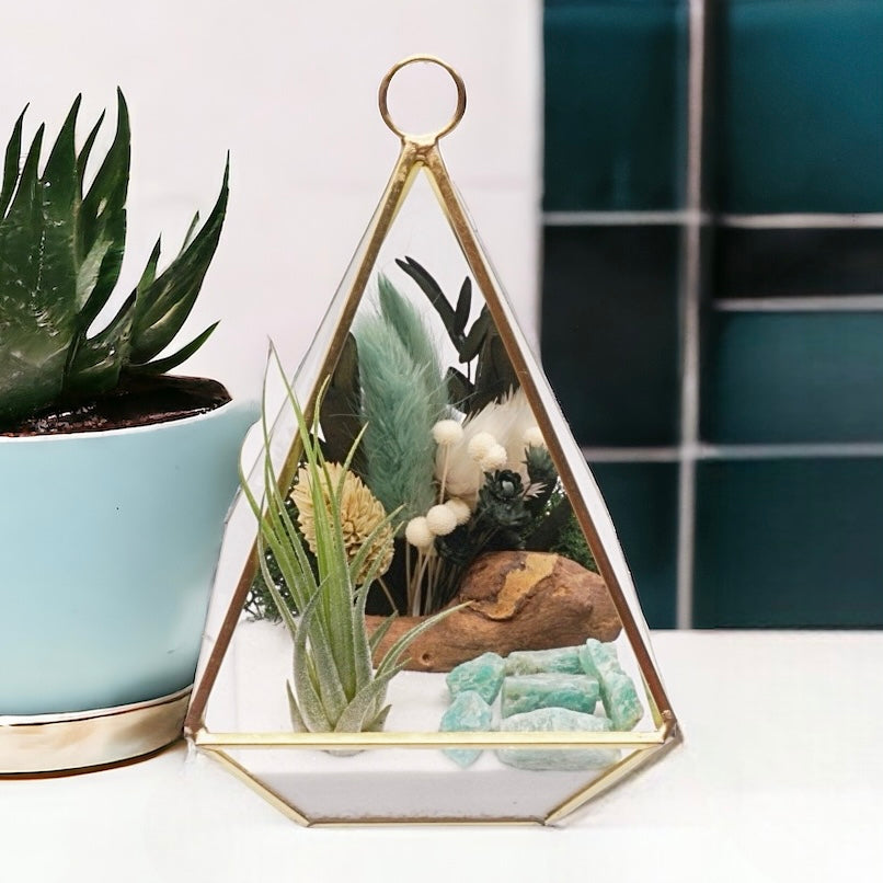 Gold-rimmed victorian glass terrarium filled with dried flowers with green accents, amazonite crystals, sand, moss, wood and an airplant