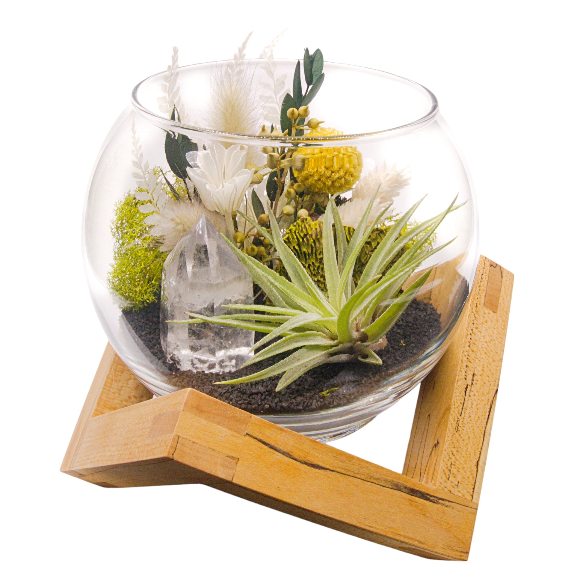 A glass bowl airplant terrarium with black sand, a bouquet of dried flowers, green moss, a dried mushroom and a crystal quartz tower.