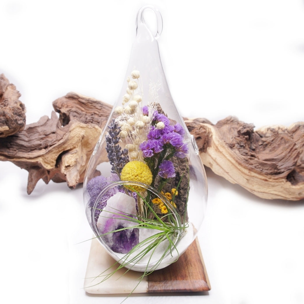 Glass teardrop terrarium with a bouquet of dried flowers with purple accents, a chevron amethyst crystal and an airplant